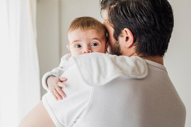 father burping his baby in bedroom, after being breastfed.