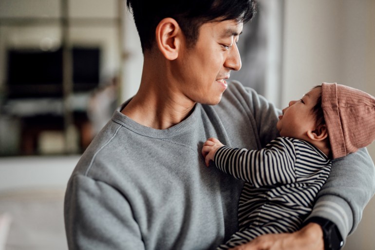 smiling asian father shot holding his baby daughter looking at each other. happy family portrait. father sharing parental responsibility.