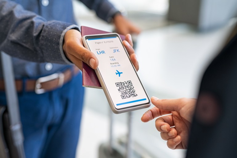 close up hand of man showing electronic boarding pass to flight attendant on phone. hostess checking electronic flight ticket at boarding gate. check in counter and online air ticket at airport. شترستوك