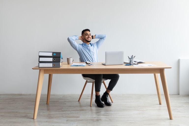 taking break. smiling young arab man relaxing on chair sitting at table and resting, using pc laptop, happy millennial male leaning back at workplace, enjoying his job, feeling pleased and satisfied ss2094203029