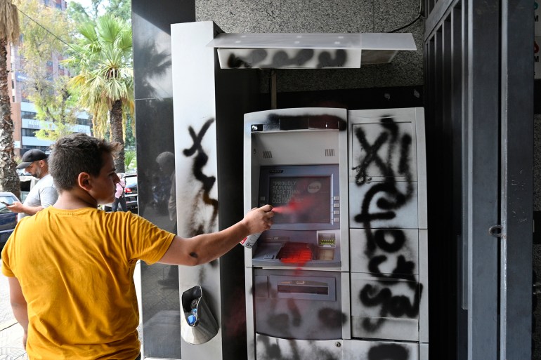 epa11570819 a protester sprays paints on an atm machine at a local bank during a protest organized by depositors' outcry, a group campaigning for the rights of depositors, in the dora area, northern beirut, lebanon, 29 august 2024. bank customers demand they be allowed to withdraw their savings, which have been blocked as a result of the ongoing economic crisis in the country, as the lebanese pound has lost about 95 percent of its value against the us dollar. the currency was trading on the parallel market at 89,500 against the dollar on 29 august, more than five times the 15,000 official rate. epa-efe/wael hamzeh