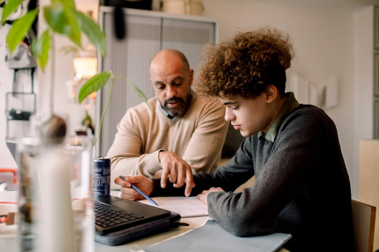 father guiding son doing homework while sitting at table - stock photo