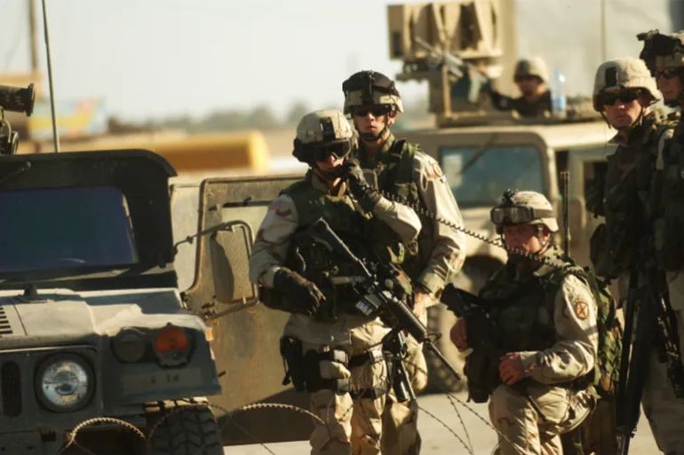 جنود أميركيون في بلدة الإسكندرية جنوب بغداد عام 2004 (غيتي) war in iraq 2003-2004 iraq - 2004: american soldiers stand guard against a hostile crowd in front of the bombed police station in the town of iskandariya, roughly 30 miles south of baghdad, iraq, february 10, 2004. a truck packed with an estimated 500 pounds of explosives blew up tuesday morning at a police station south of baghdad as dozens of would-be recruits lined up to apply for jobs, and a hospital official said at least 50 people were killed and 50 others wounded. (photo by lynsey addario/getty images reportage)