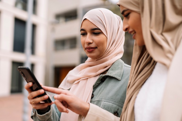 portrait of two arab female friends using a smartphone together while standing outdoors on the street.