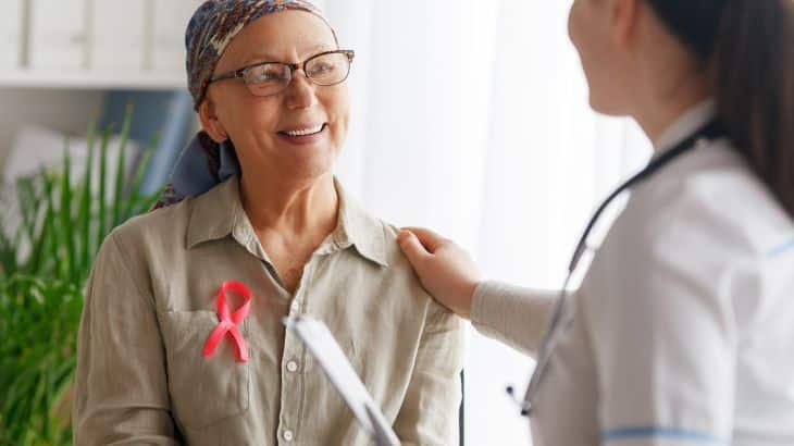 Pink ribbon for breast cancer awareness. Female patient listening to doctor in medical office. Support people living with tumor illness.