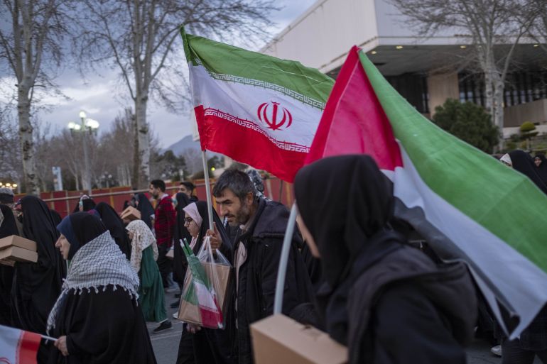 a man and a veiled woman are carrying packs of meals and iranian and palestinian flags as they leave the azadi (freedom) stadium after participating in a religious gathering to commemorate the holy month of ramadan in western tehran, iran, on march 26, 2024.