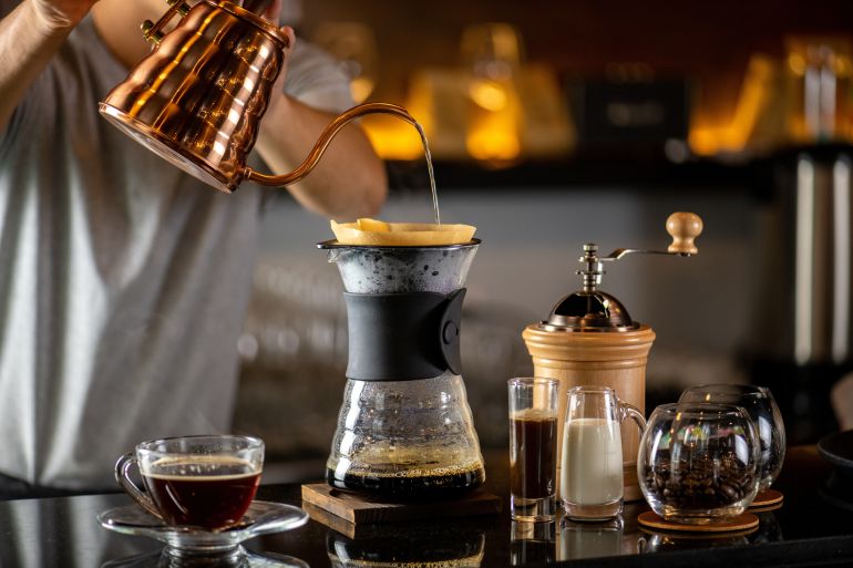 barista preparing drip coffee with a filter from a copper pot