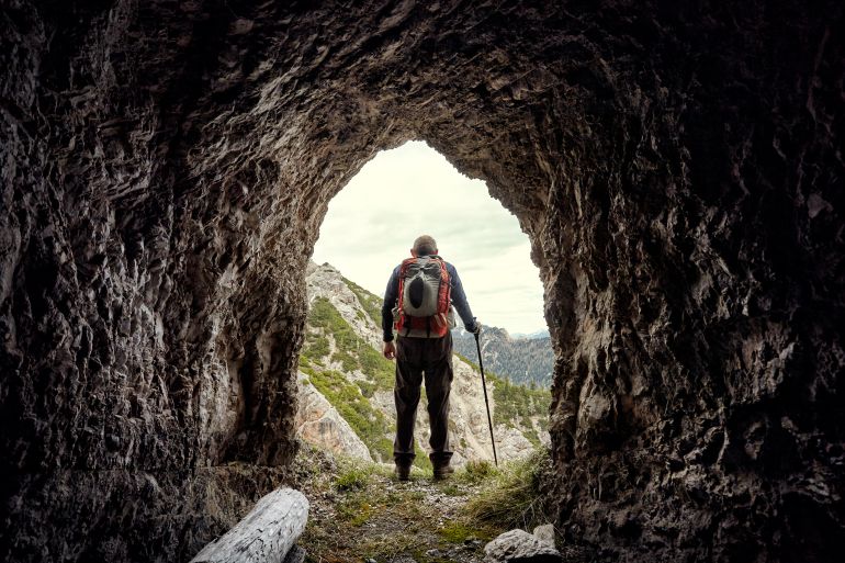 hiker seen through mountain tunnel, dolomites, italy