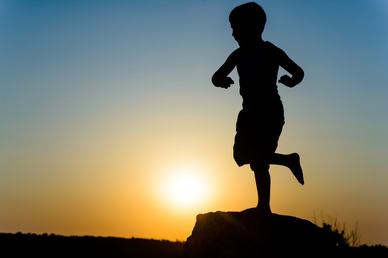 young boy silhouetted by the sunset standing balancing on one leg against the fiery orange orb of the sun in a twilight sky; shutterstock id 289645370; purchase_order: aj; job: ; client: ; other: