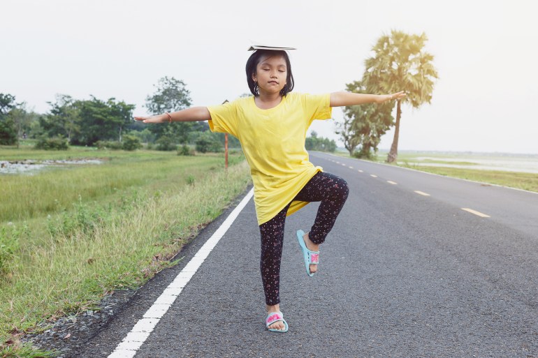 cute kid girl playing standing legs and arms one side. with the book is placed on the head to create a balance.; shutterstock id 484067182; purchase_order: aj; job: ; client: ; other: