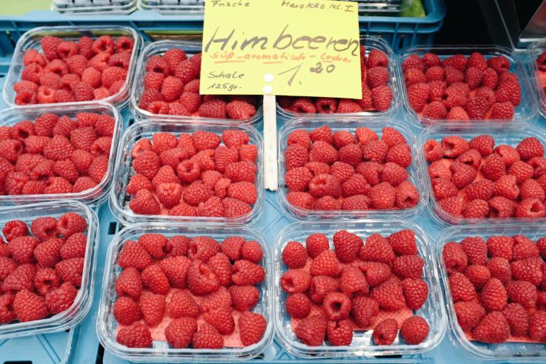 plastic containers with fresh raspberries on market stall