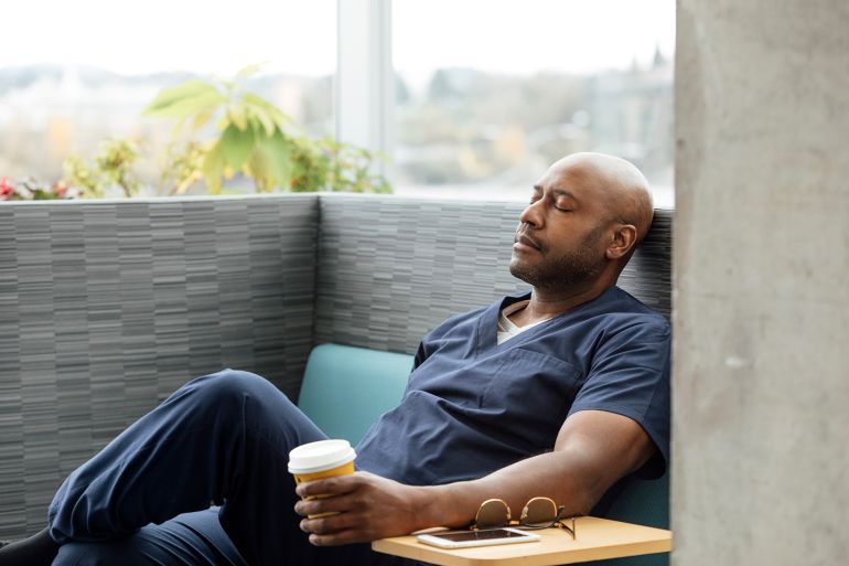 male nurse with disposable cup resting on sofa in hospital - stock photo