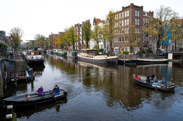 People navigate small boats on the Lekkersluis canal in Amsterdam on October 23, 2024, as the city launches its 750th anniversary celebrations.