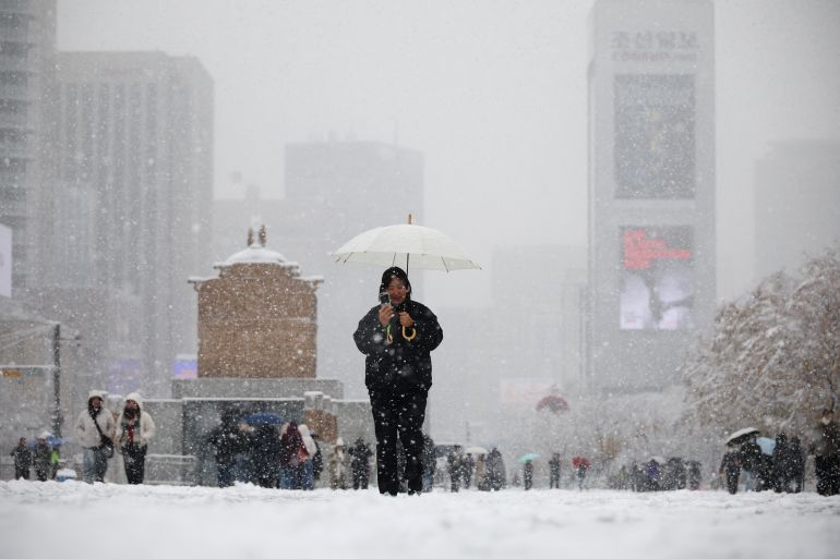 A woman using a smart phone walks during heavy snow fall in central Seoul, South Korea, November 27, 2024. REUTERS/Kim Hong-Ji