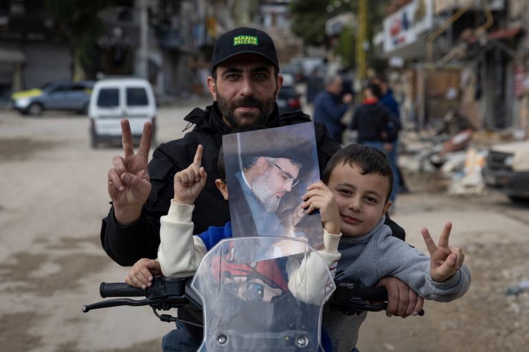 A man and his son gesture as they hold a picture of late Hezbollah leader Sayyed Hassan Nasrallah, in the southern Lebanese town of Nabatieh, on the second day of the ceasefire between Israel and Hezbollah, Lebanon November 28, 2024. REUTERS/Adnan Abidi