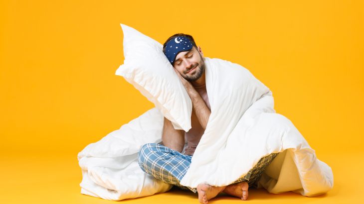 Full length of smiling young bearded man in pajamas home wear sleep mask sitting with pillow blanket isolated on bright yellow colour background studio portrait. Relax good mood lifestyle concept; Shutterstock ID 1885457752; purchase_order:aja; job:; client:; other: