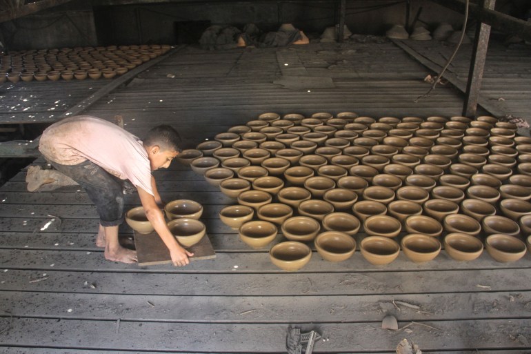 A person carries pots as Palestinians work in a pottery workshop to respond to an increase in the demand for clay pots used to cool water due to power cuts and hot weather, according to workers, amid the Israel-Hamas conflict, in Gaza City August 13, 2024. REUTERS/Mahmoud Issa