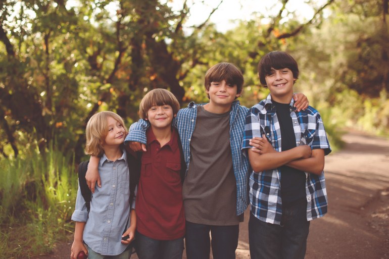 Four brothers on the way to school. Looking into camera, smiling, happy, wearing back packs.