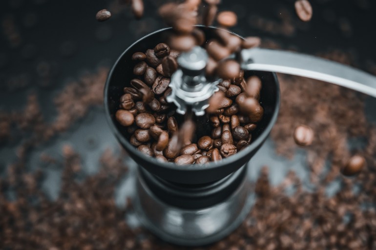 Fried coffee beans are falling to the manual grinder. Cinematic dark colors. Preparation of fresh beverage morning coffee for breakfast. Mill for grinding. Isolated on black background.