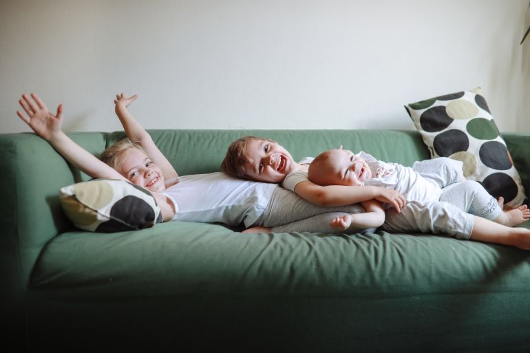 Three emotional sibling children together on green sofa at home. Sincere authentic photo and copy space.