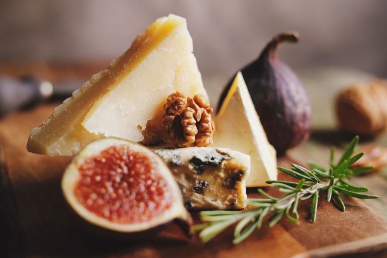 Different cheeses with fig and walnut on cutting board.