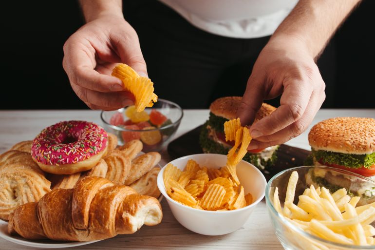 Unhealthy snack, junk food, compulsive overeating. Man overeating unhealthy meals taking hamburger and potato chips from plate