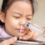 Little asian girl saline nasal wash nose at home. Asia mother making nasal wash for her kid girl by flushing nose cleaning with syringe and saline to treat the flu. health care medical people concept.