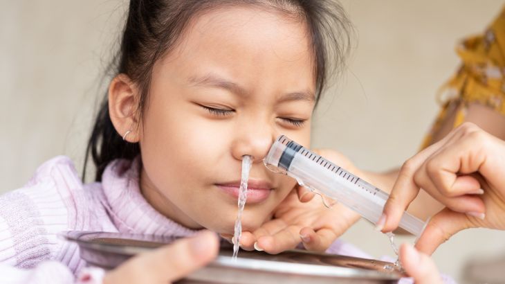 Little asian girl saline nasal wash nose at home. Asia mother making nasal wash for her kid girl by flushing nose cleaning with syringe and saline to treat the flu. health care medical people concept.