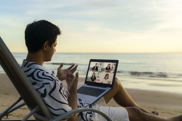 Asian business man having remote video conference call with his business team at the beach during vacation in holiday.