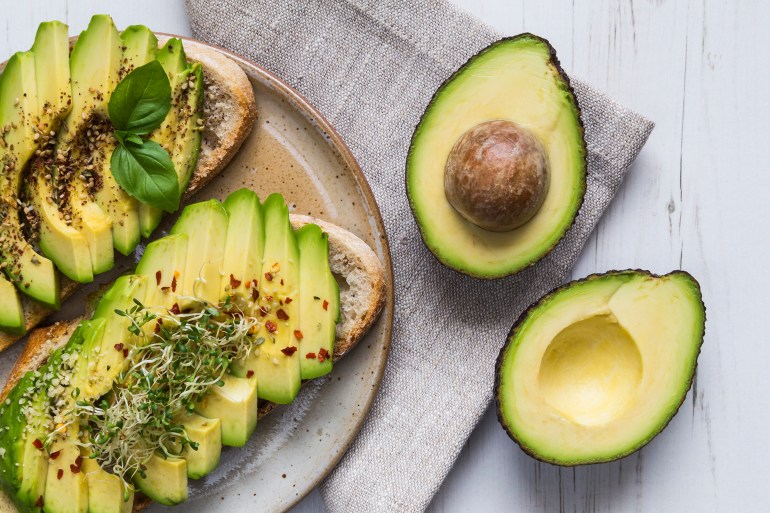 Toast with sliced avocado topping, basil leaf and seasoning.