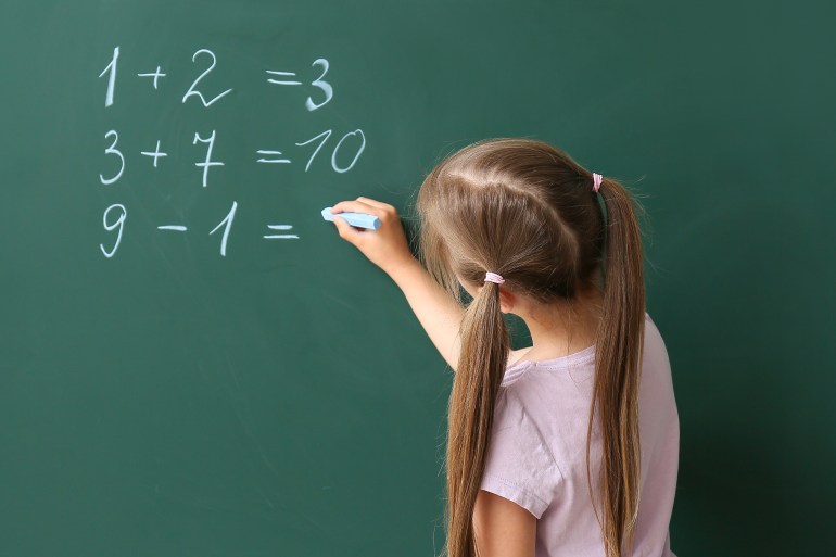 Cute little schoolgirl writing on blackboard during math lesson ; Shutterstock ID 2314040705; purchase_order: aljazeera ; job: ; client: ; other: