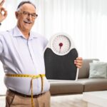 Happy mature man with a weight scale and a measuring tape gesturing thumbs up