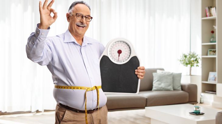 Happy mature man with a weight scale and a measuring tape gesturing thumbs up