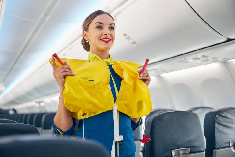 Stewardess in the cabin of the passenger airplane doing training of instruction on safety measures in the event of an emergency before the flight