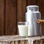 A glass of milk with a milk churn