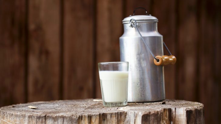 A glass of milk with a milk churn